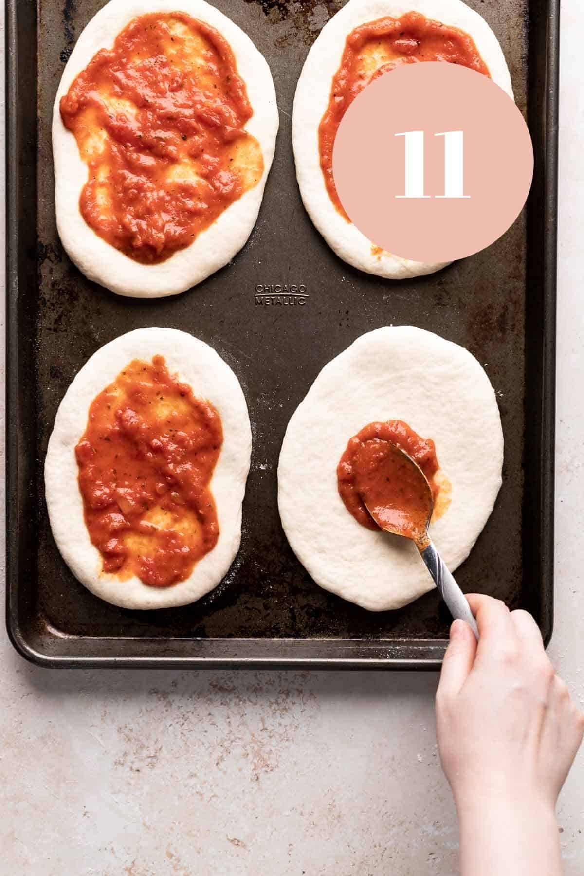 topping the chewy pizza dough with sauce.