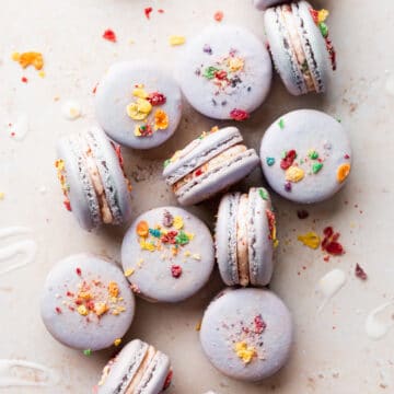 a bunch of macarons sitting on a cream colored surface surrounded by cereal