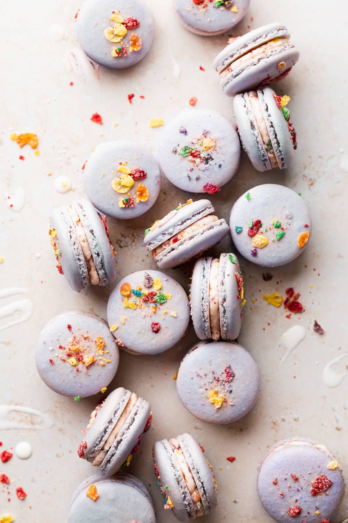 a bunch of macarons sitting on a cream colored surface surrounded by cereal