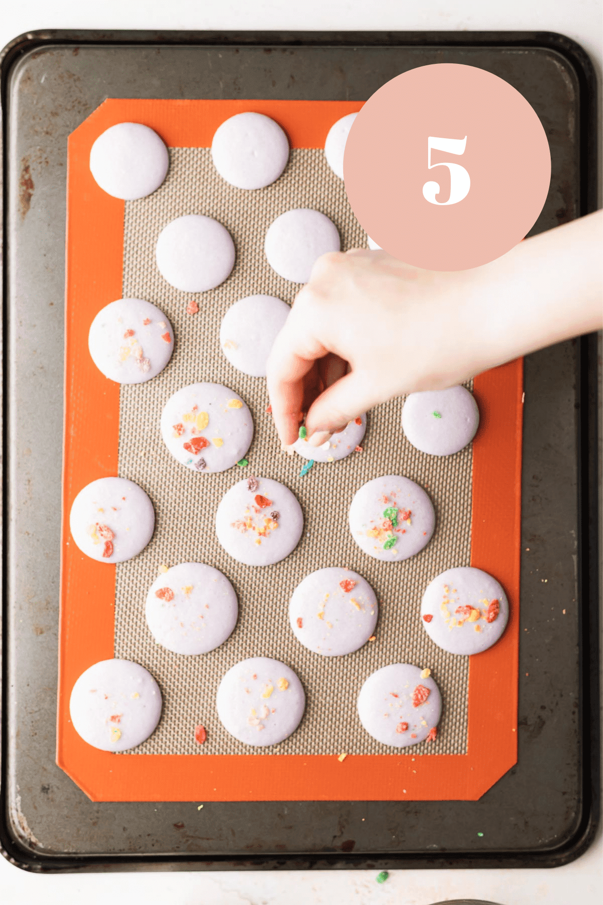 overhead shot of someone sprinkling cereal on the macaron shells