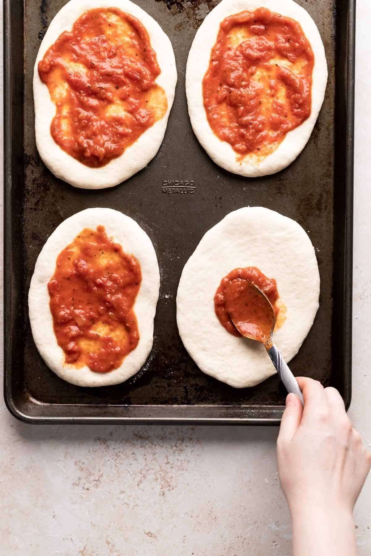 spooning the homemade san marzano pizza sauce on dough.