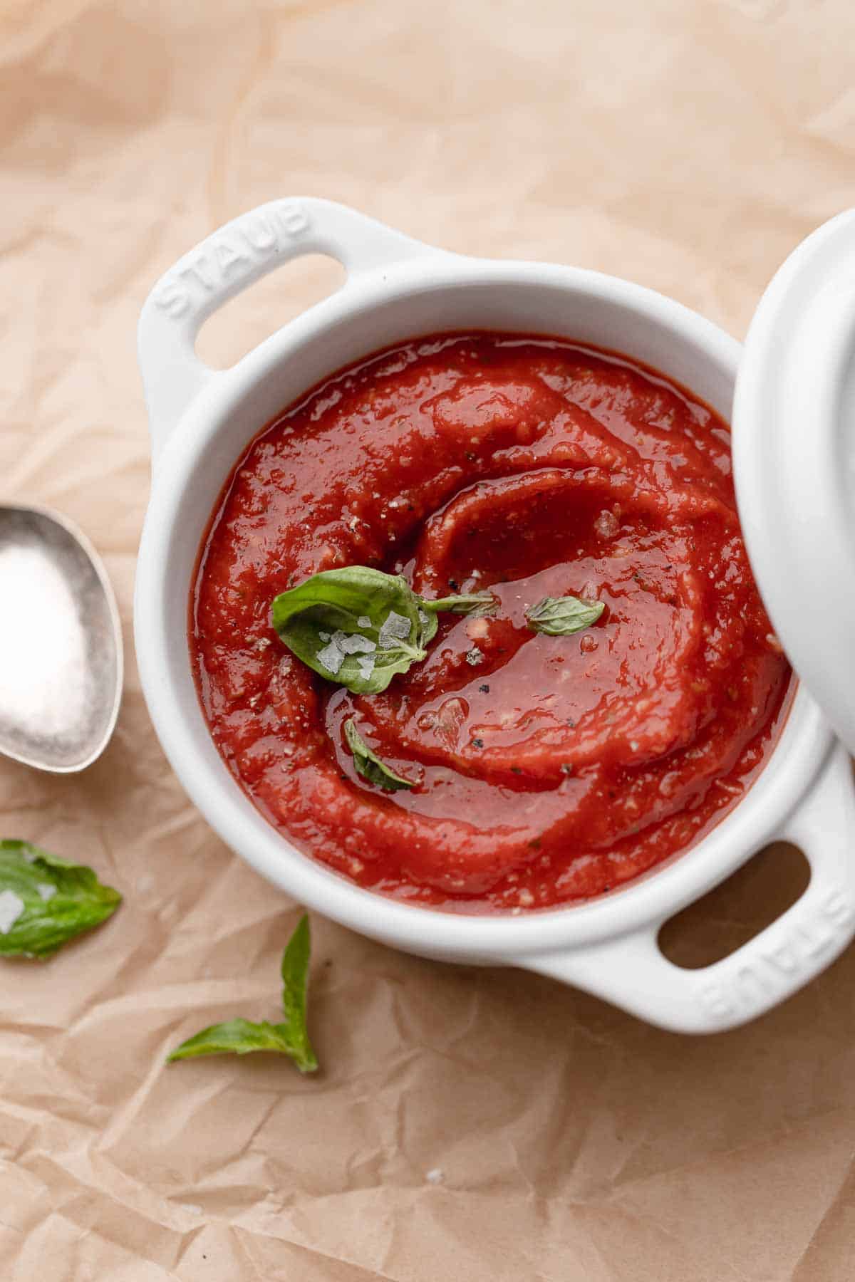 homemade san marzano pizza sauce in a small pot garnished with fresh basil and sea salt.