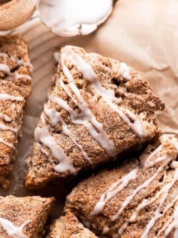 apple cinnamon scones on parchment paper drizzled with glaze.