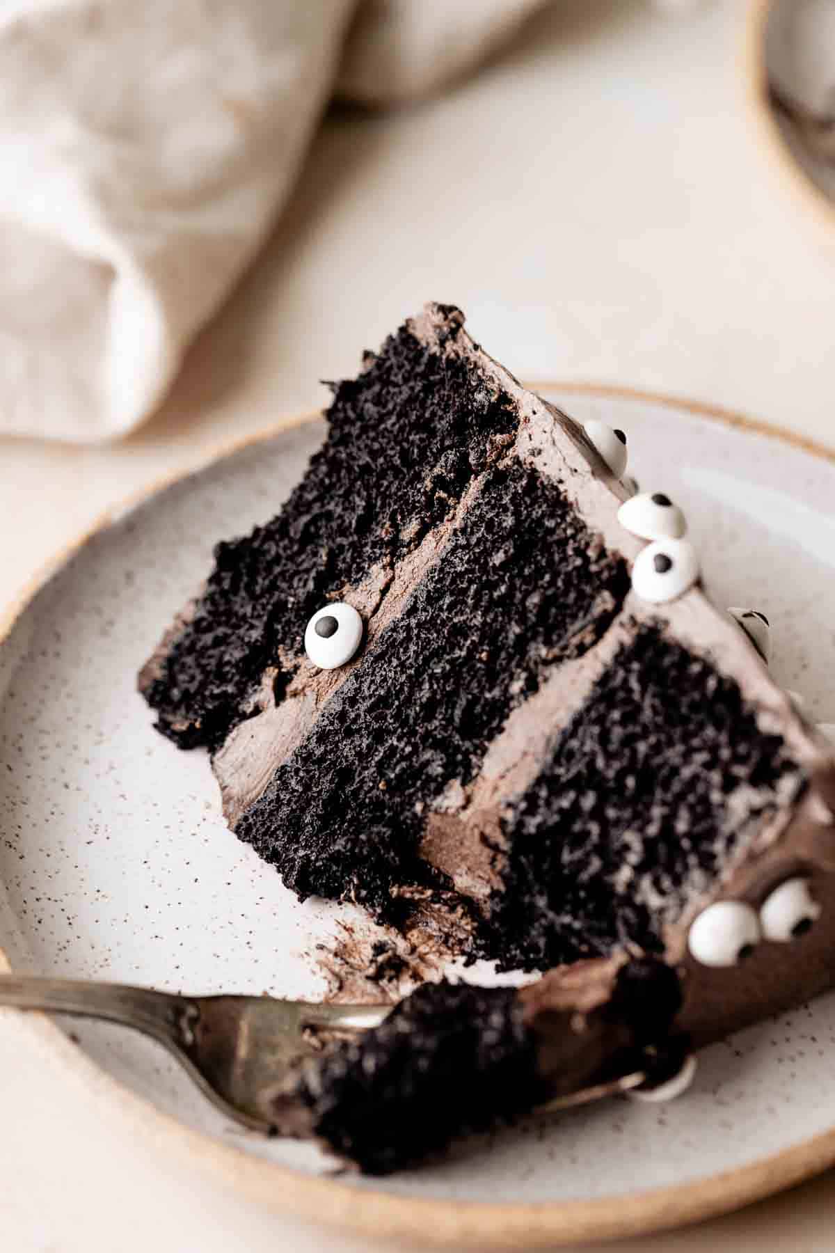 a slice of moist chocolate cake with black cocoa buttercream on a plate.