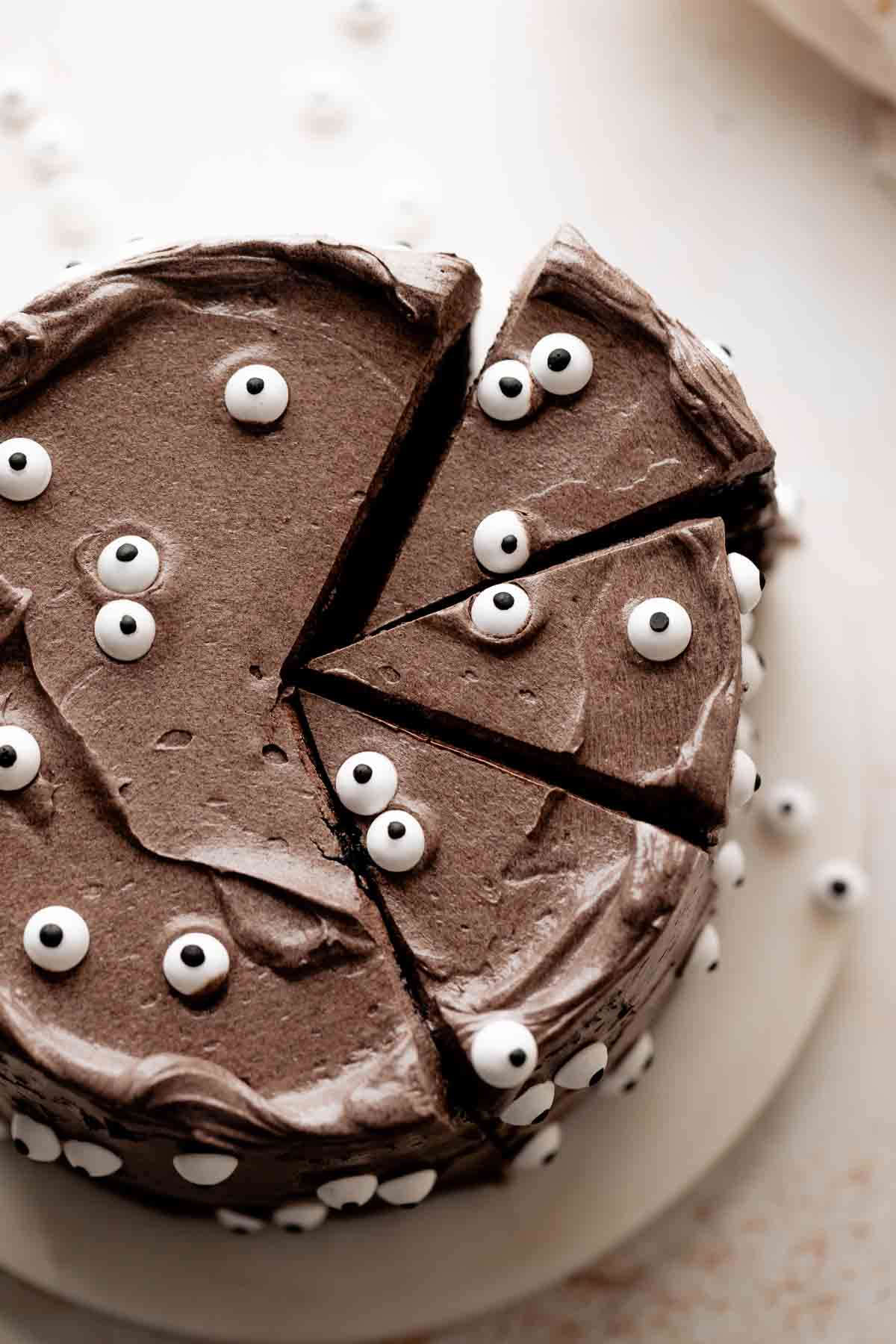 black velvet cake with three slices cut out decorated with eyeball candies.