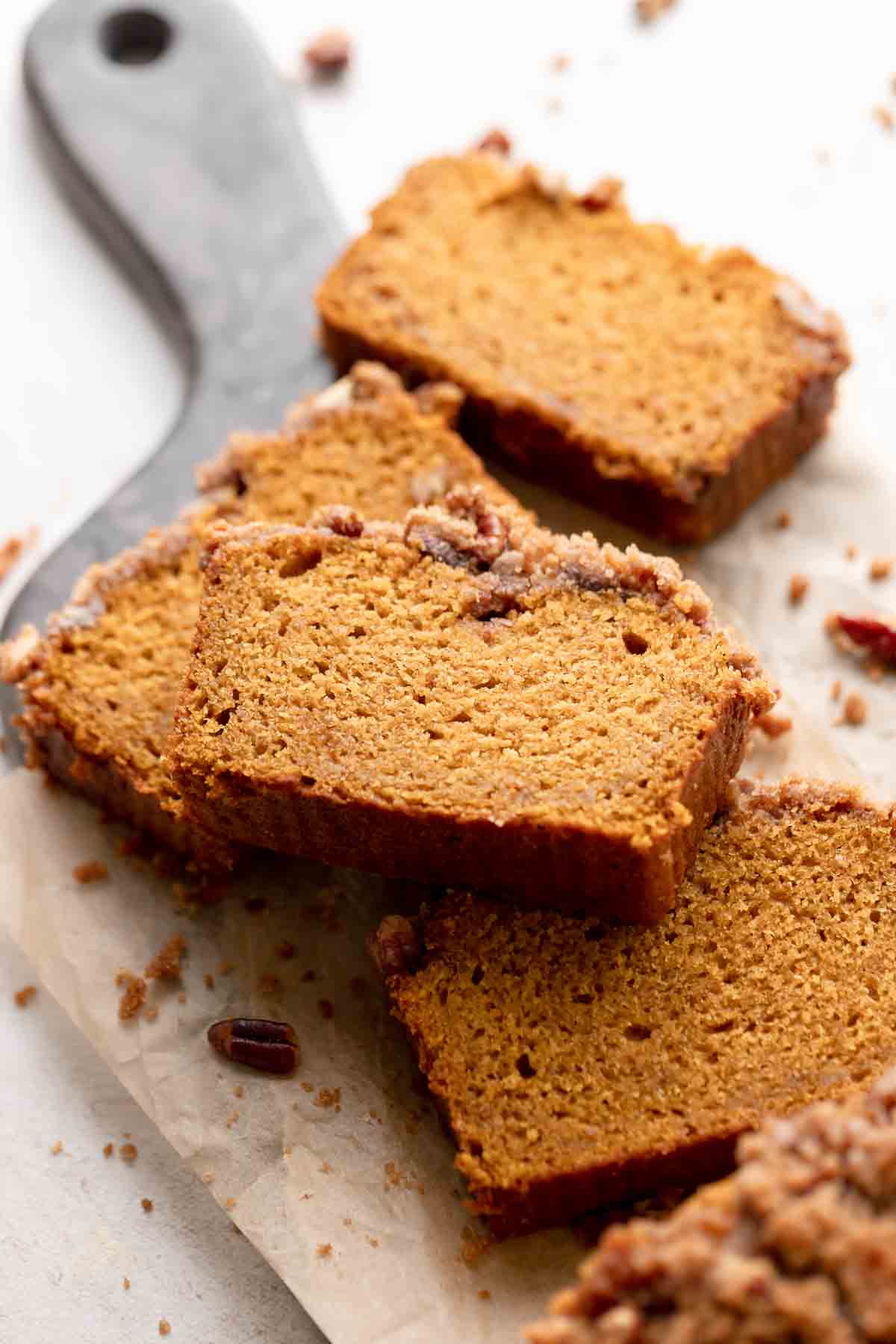 slices of cinnamon pecan pumpkin bread on parchment with streusel topping scattered around.