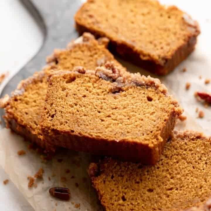 slices of cinnamon pecan pumpkin bread on parchment with streusel topping scattered around.