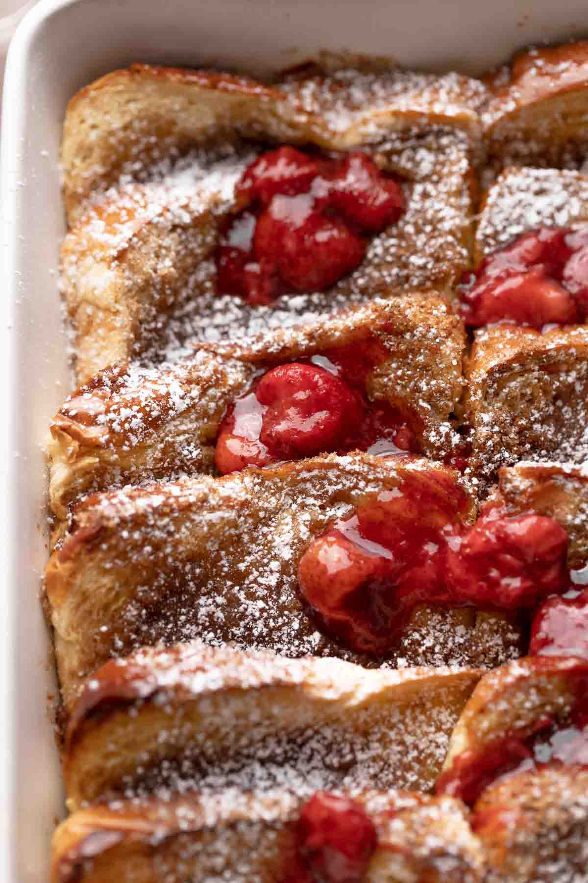 brioche french toast casserole dusted with powdered sugar and strawberries.