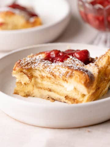 a slice of brioche french toast casserole on a plate dusted with powdered sugar.