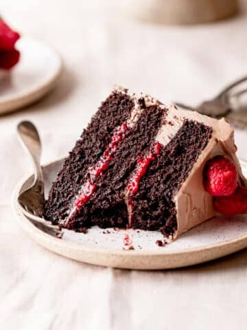 a slice of chocolate raspberry cake on a plate with fresh raspberries.