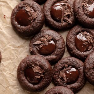 chocolate thumbprint cookies in a pile on a piece of brown parchment paper.