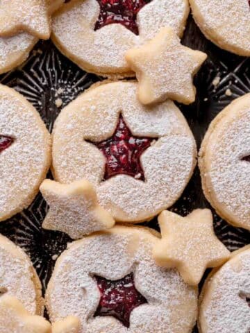 linzer tart cookies with raspberry jam on a black baking tray.