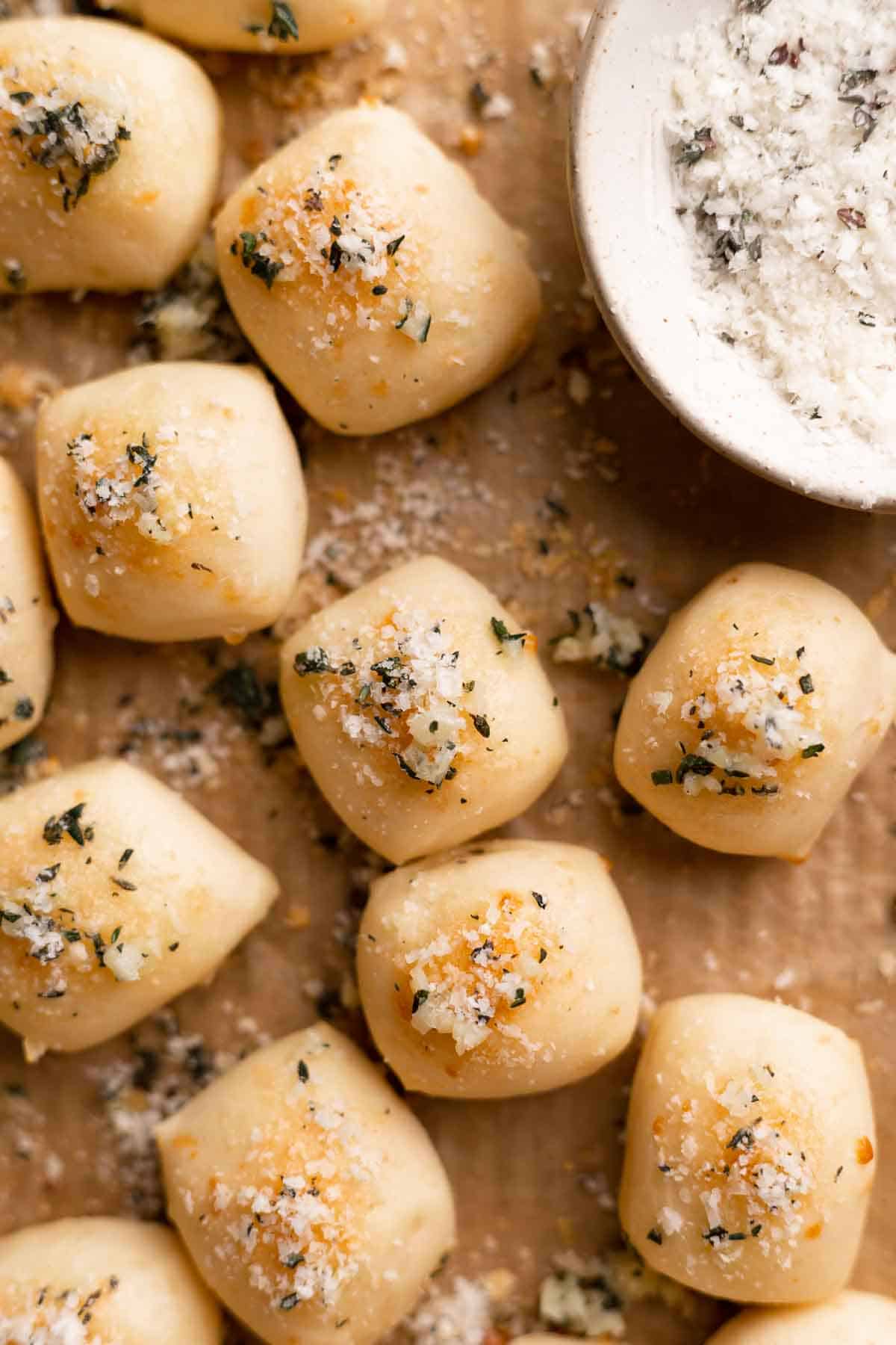 parmesan bread bites on a baking sheet sprinkled with parmesan cheese and garlic butter.