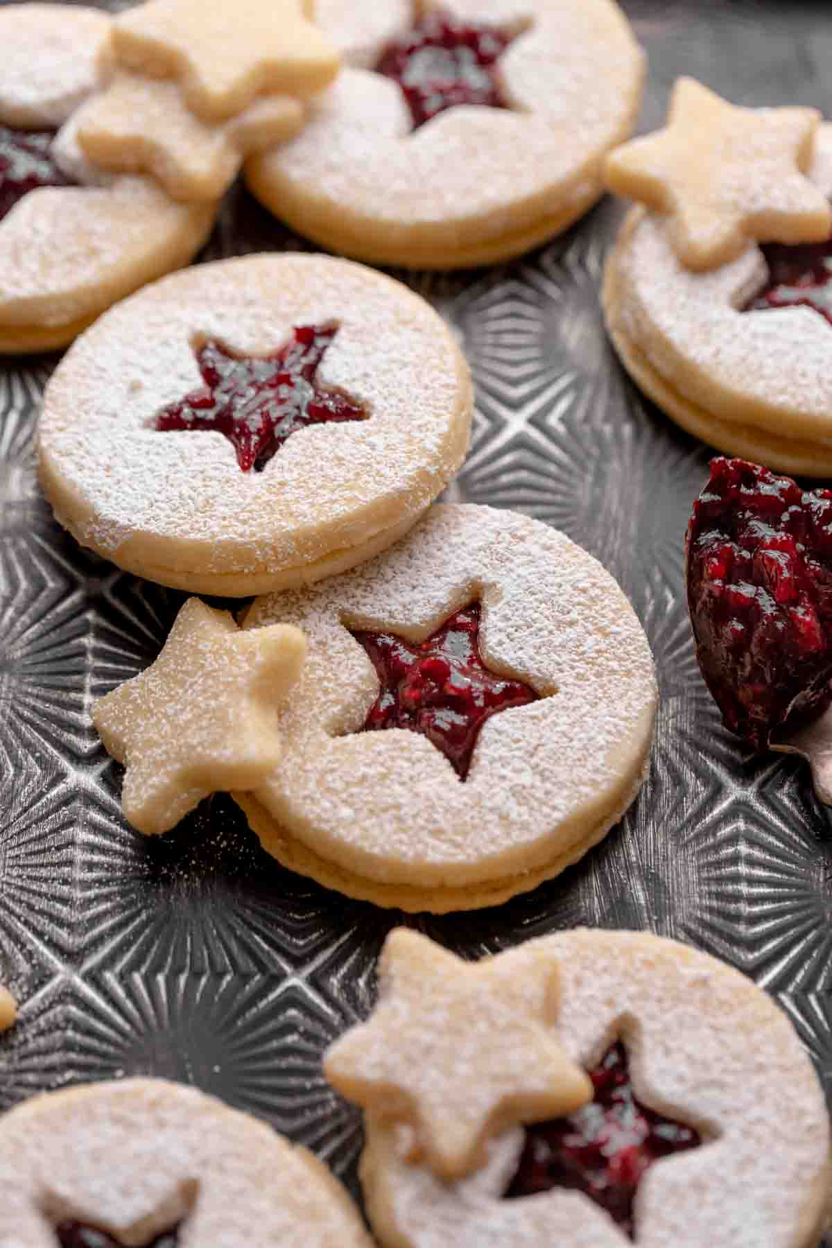 raspberry linzer cookies filled with jam and dusted with powdered sugar on a black tray.