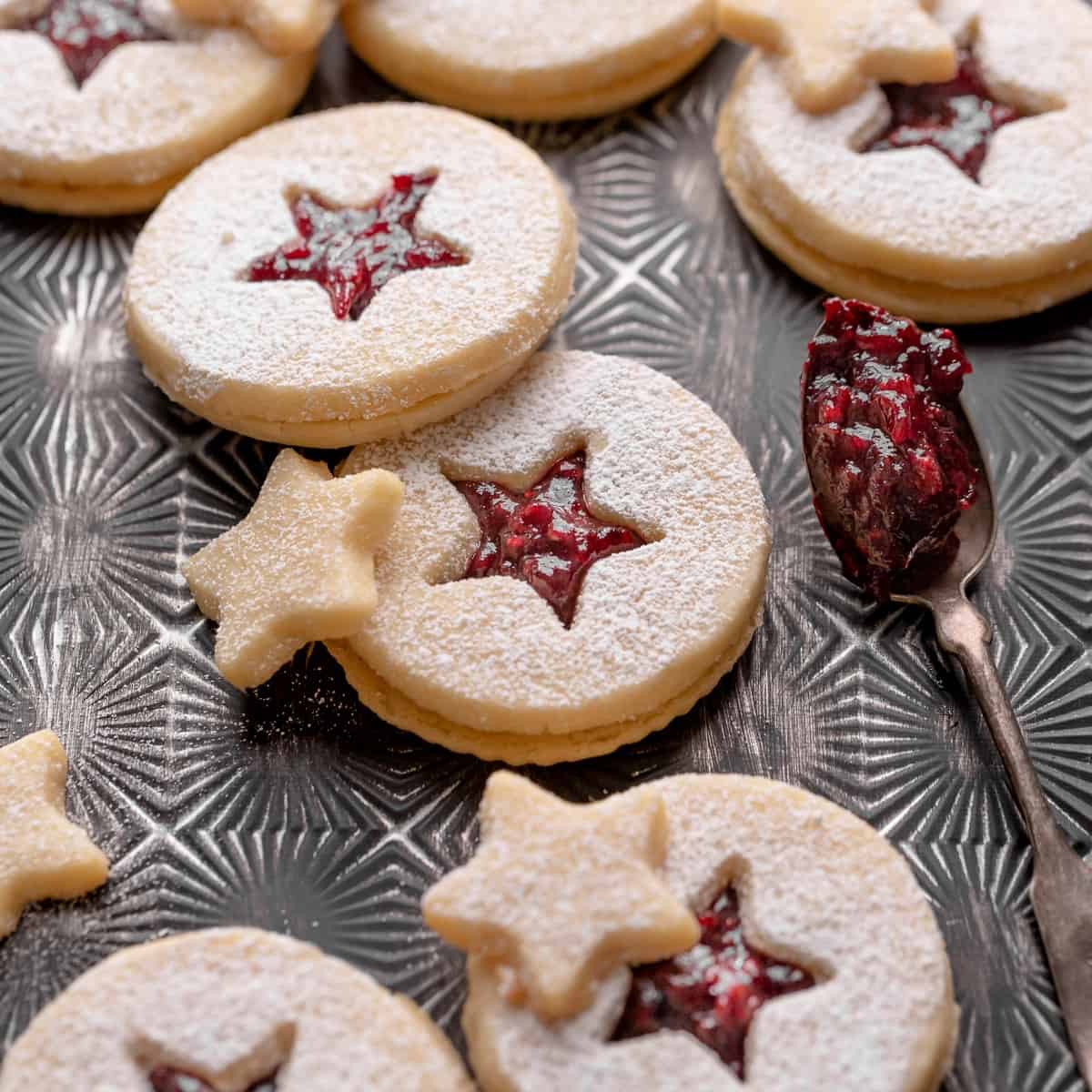 shortbread linzer cookies with raspberry jam on a black tray.