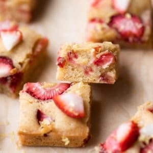 strawberry lemon blondies on brown parchment paper topped with fresh strawberries and lemon zest.