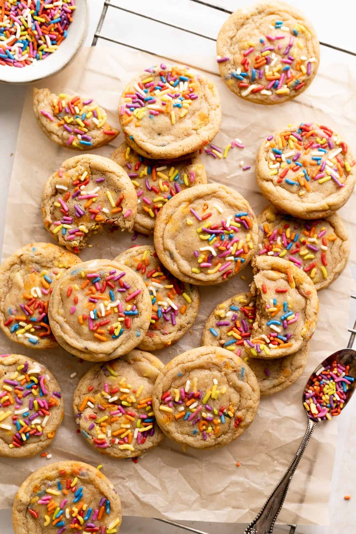 birthday cake cookies covered in rainbow sprinkles on brown parchment paper.