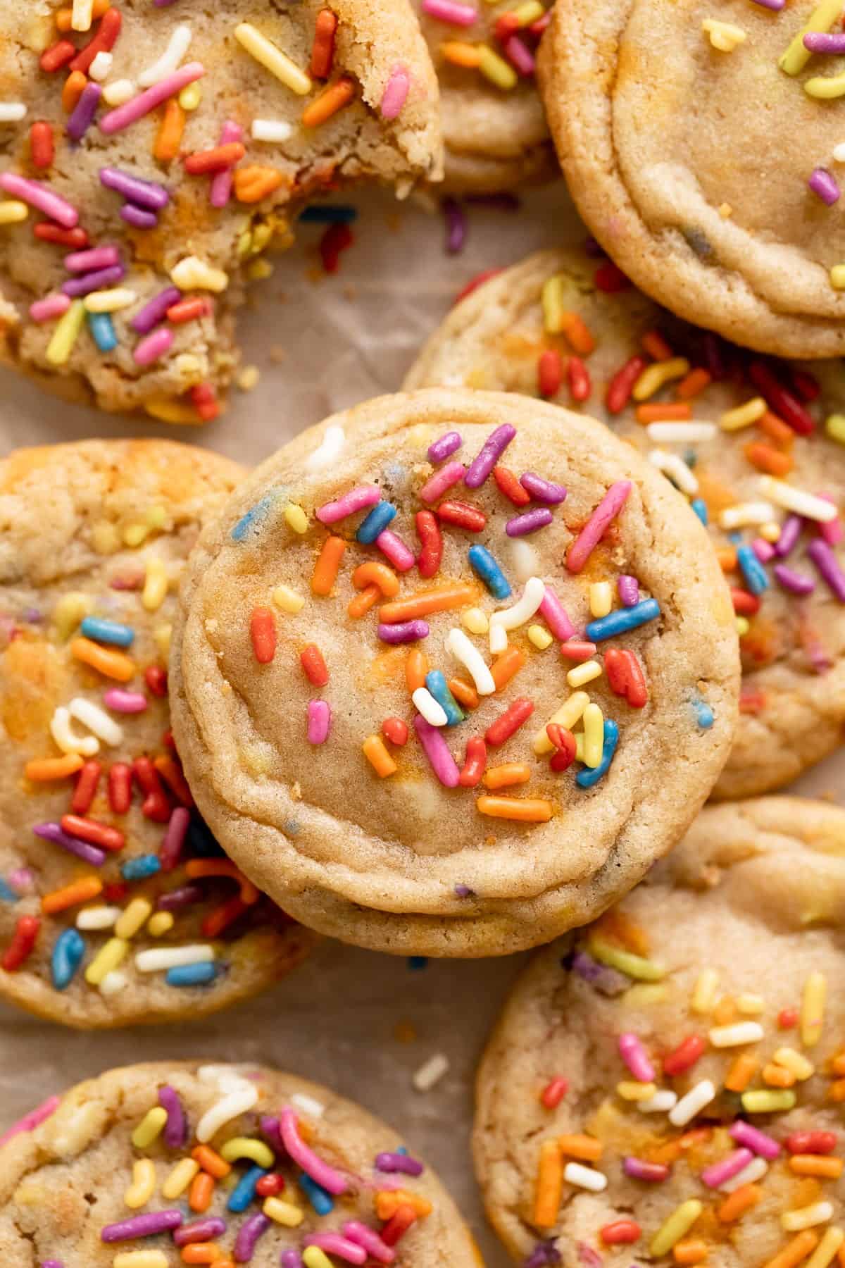 birthday cake cookies topped with rainbow sprinkles on a baking tray.