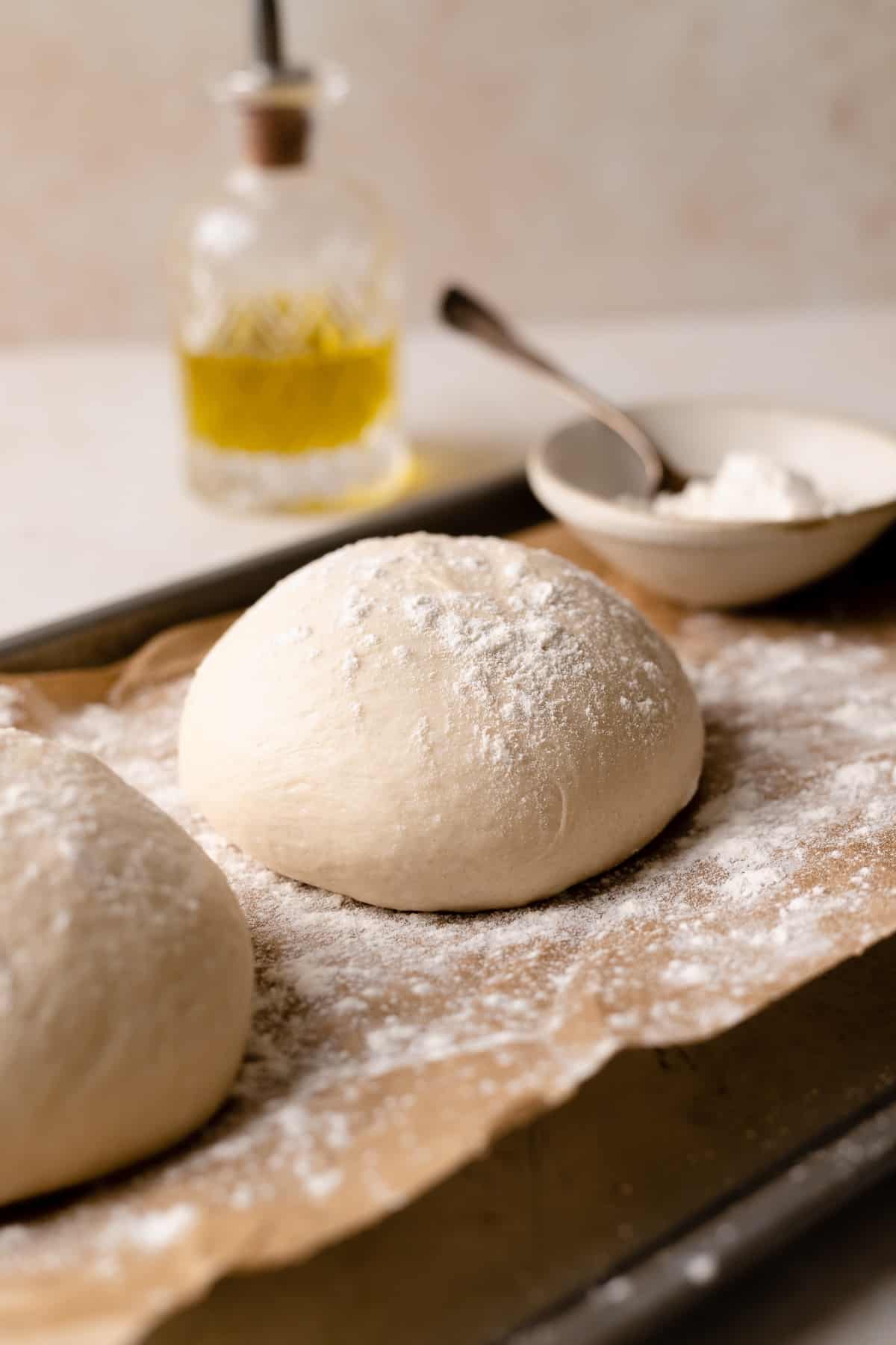 two balls of homemade pizza dough on a baking tray dusted with flour.