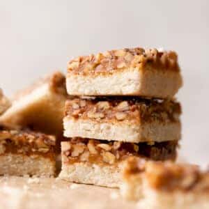 caramel pecan bars in a stack on parchment paper.