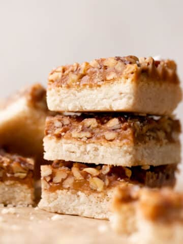 caramel pecan bars in a stack on parchment paper.
