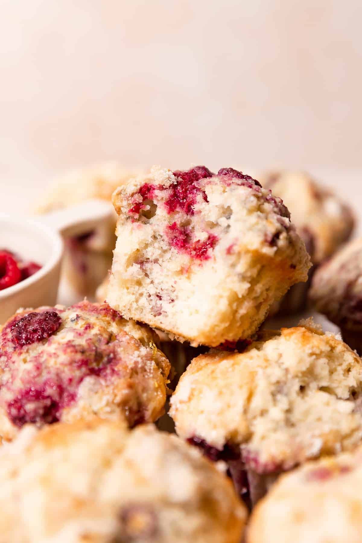 A pile of lemon raspberry muffins with the top one missing a bite to show the fluffy texture.