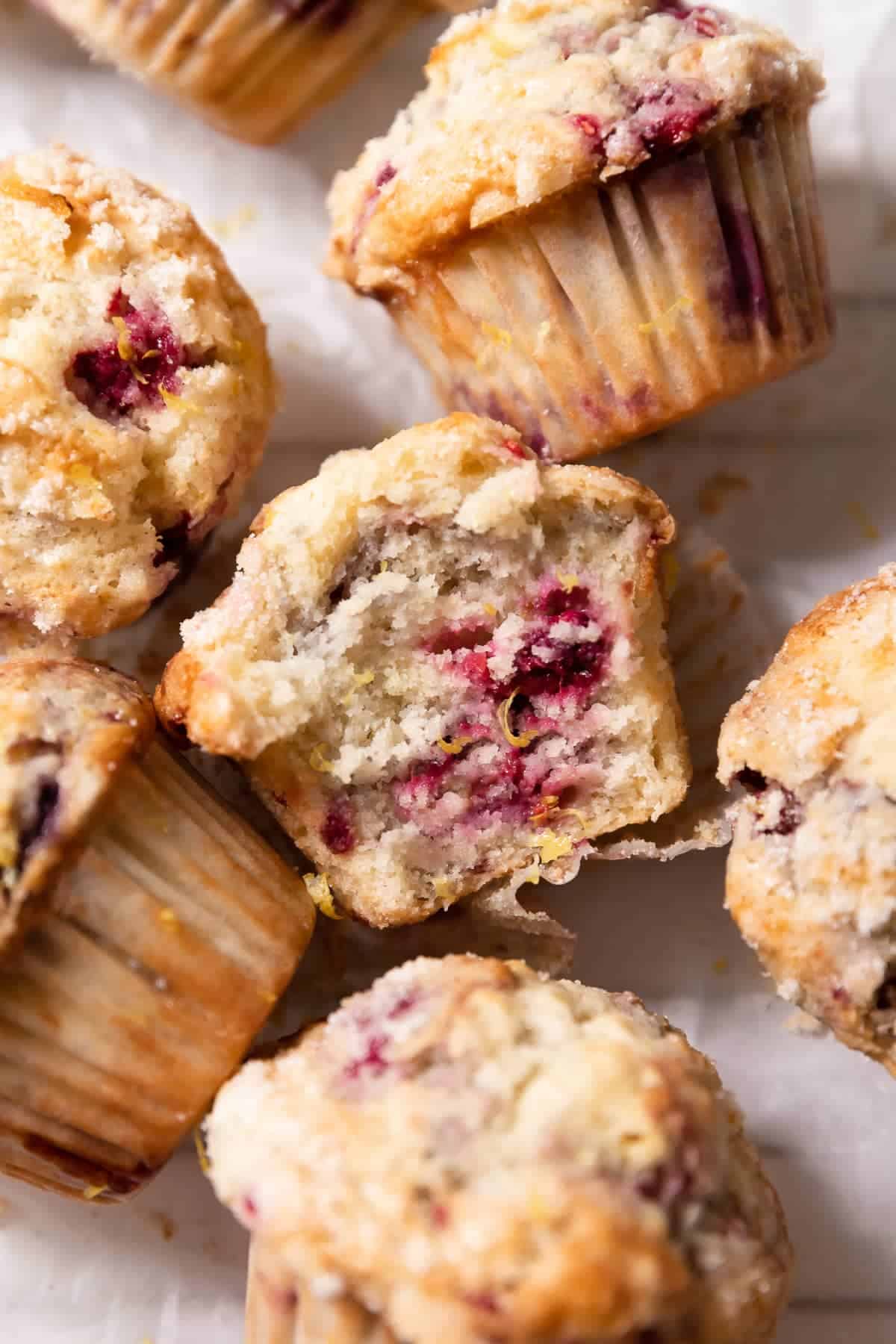 A raspberry muffin on its side with a bite taken out of it covered in fresh lemon zest.