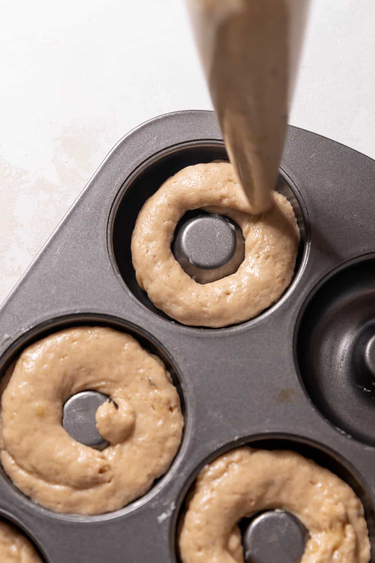 piping the donut batter into a donut pan.