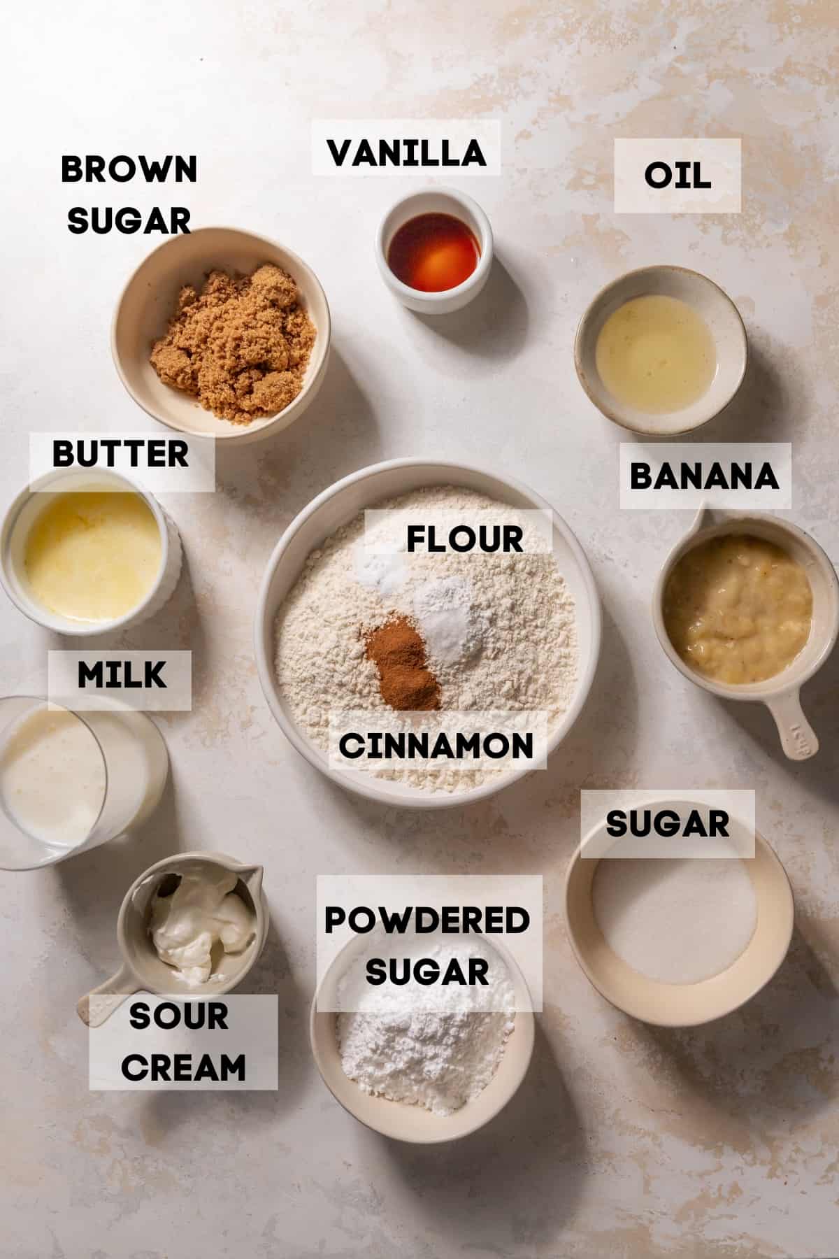 ingredients needed to make banana donuts in bowls with labels.