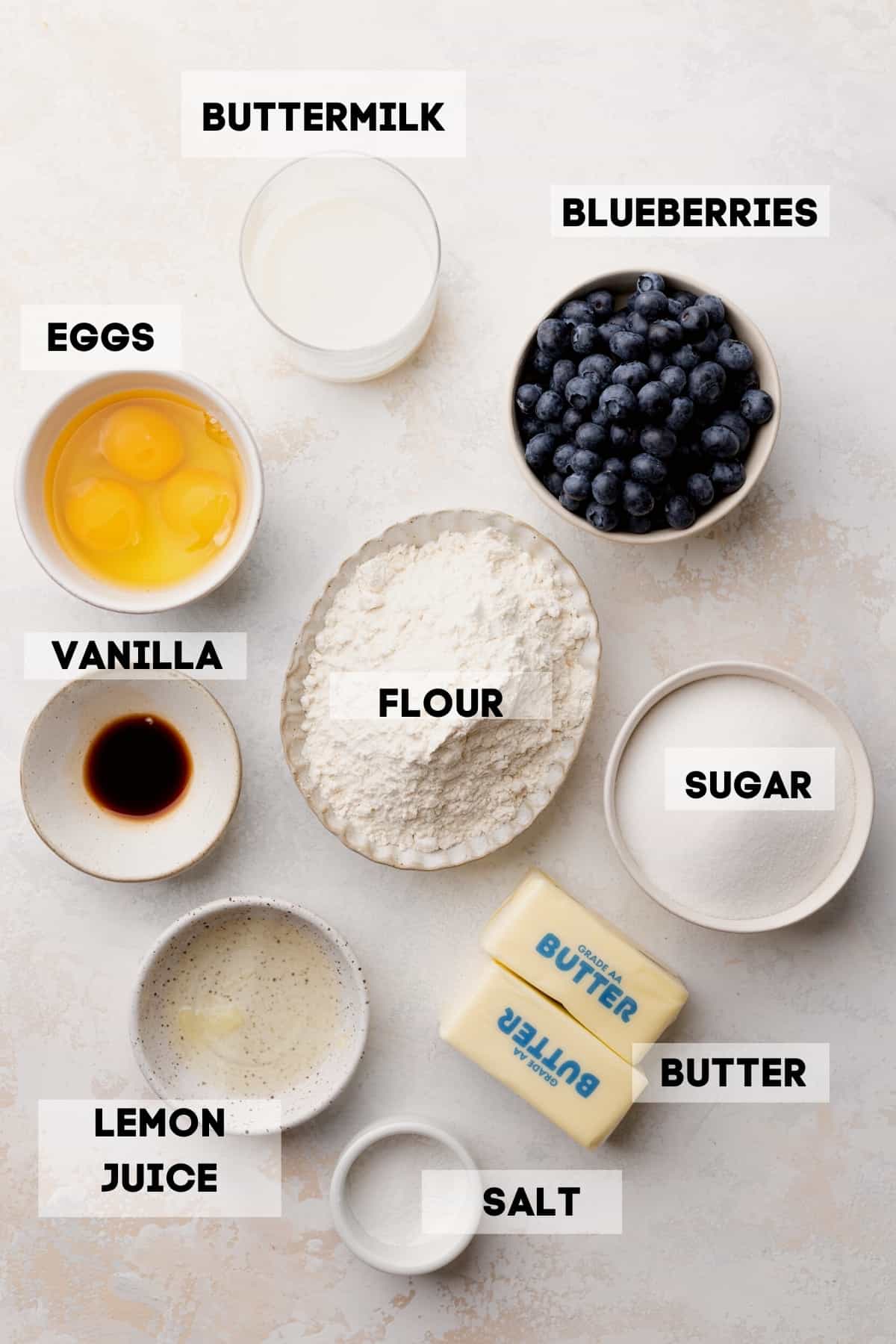 ingredients needed to make blueberry cake in bowls with labels.