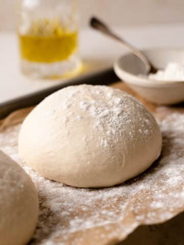 chewy pizza dough ball on parchment paper dusted with flour.
