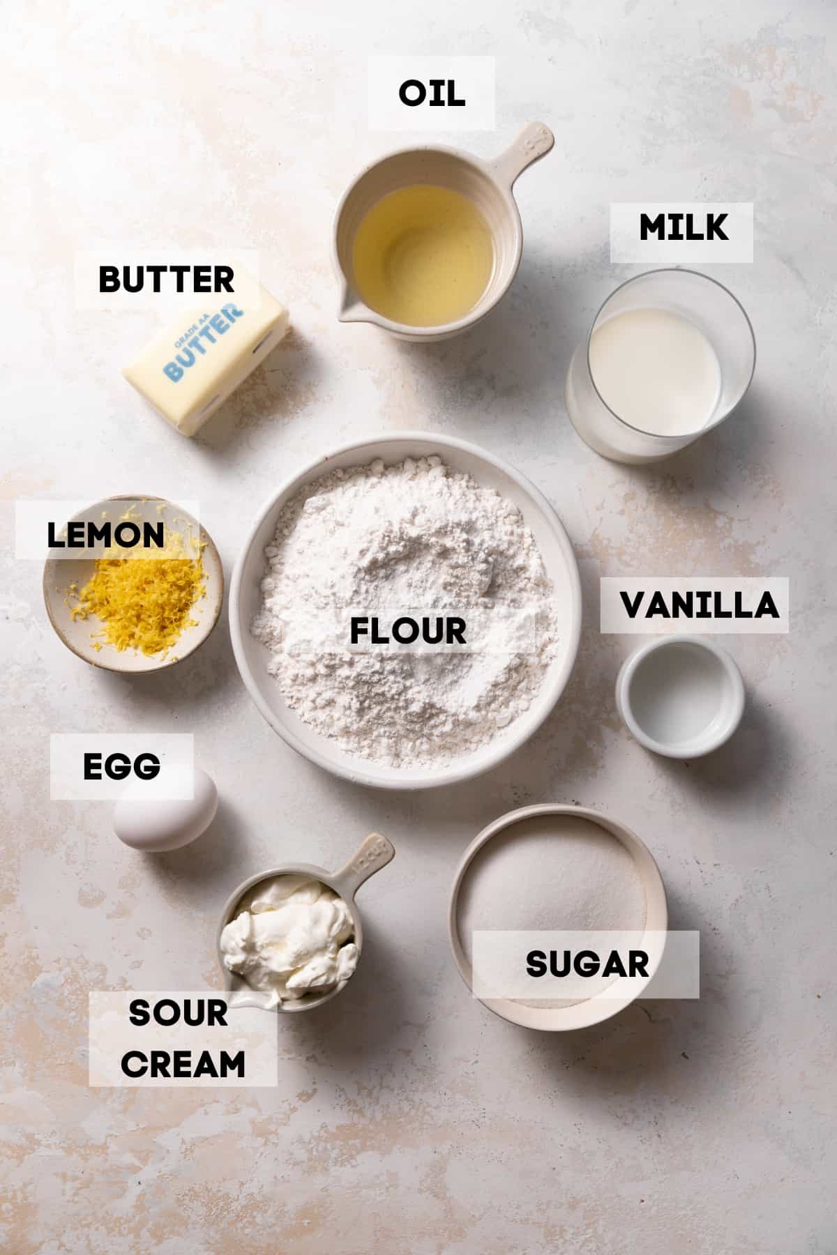 ingredients needed to make lemon cake in bowls with labels.