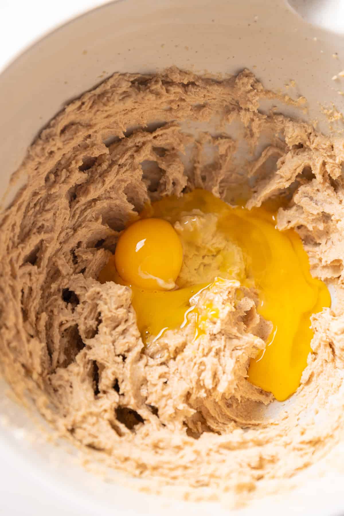 egg being mixed into the sugar and butter in a mixing bowl.
