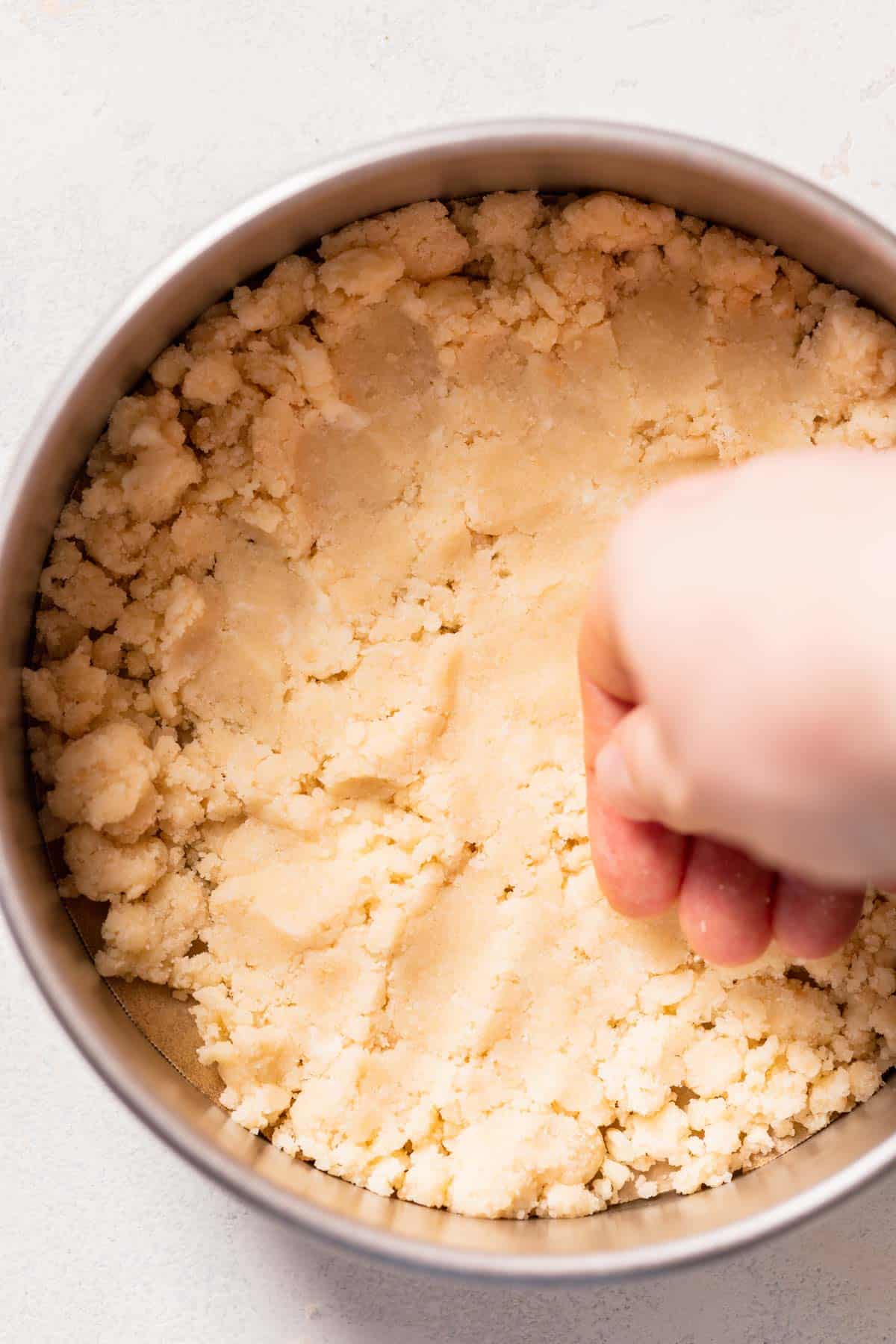 a hand pressing shortbread crust into a cake pan.
