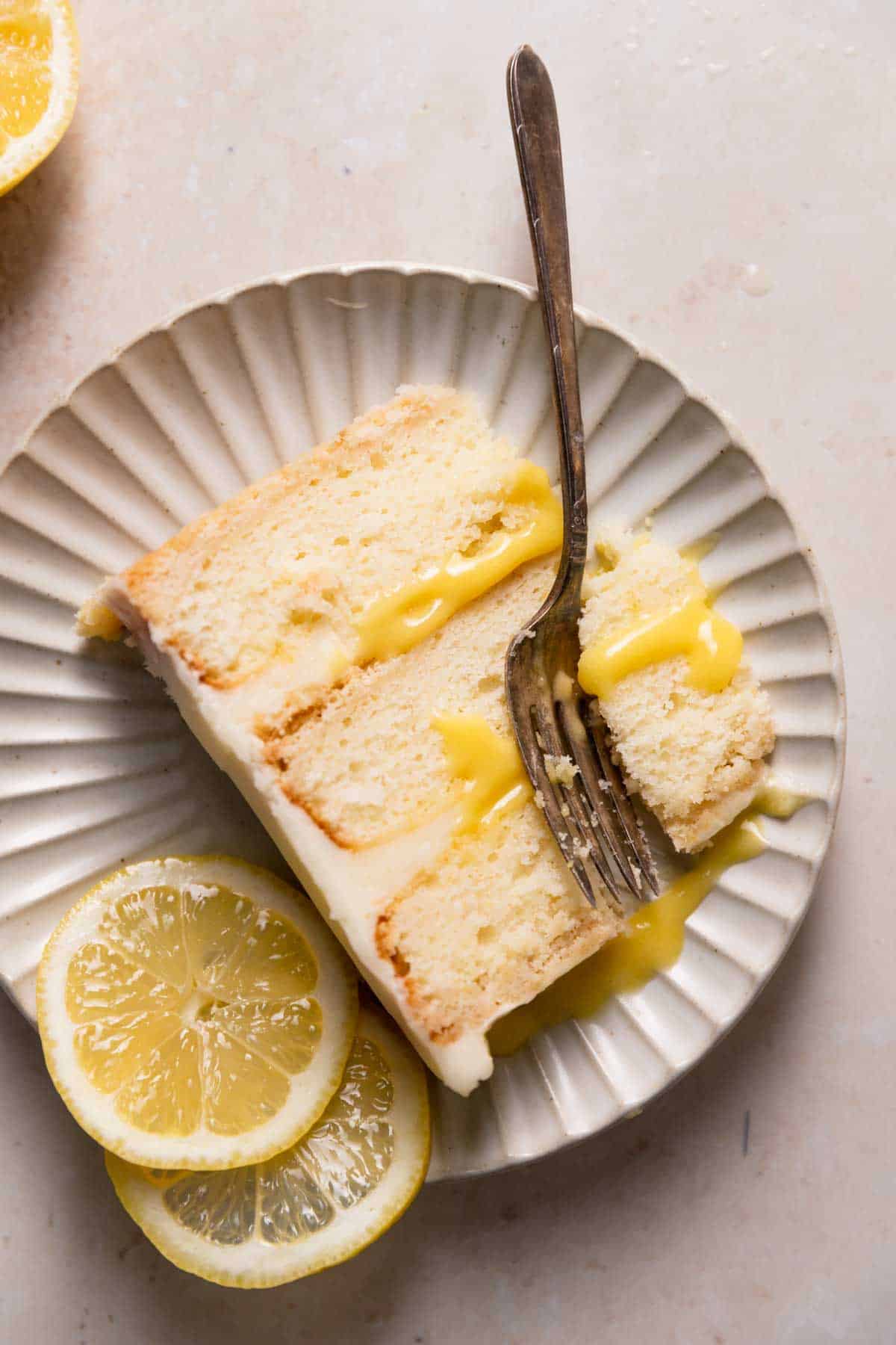 a slice of lemon bar cake on a white plate with fresh lemon slices.