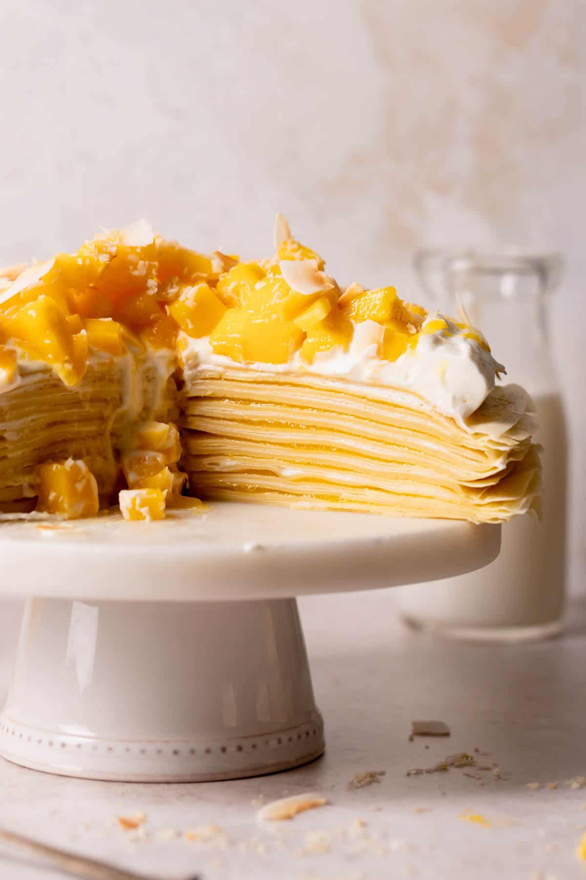 mango crepe cake on a cake stand with whipped cream and chopped mango.