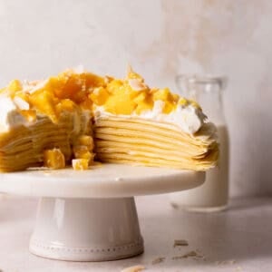 mango crepe cake topped with whipped cream on a cake stand.