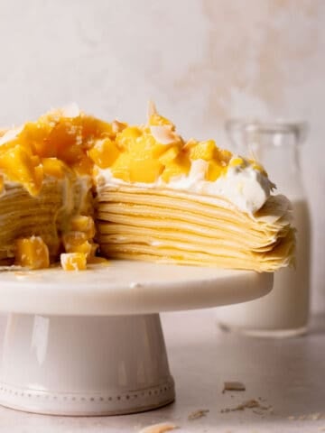 mango crepe cake topped with whipped cream on a cake stand.