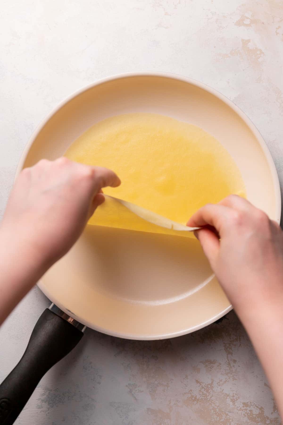 two hands flipping the crepe over in the pan.