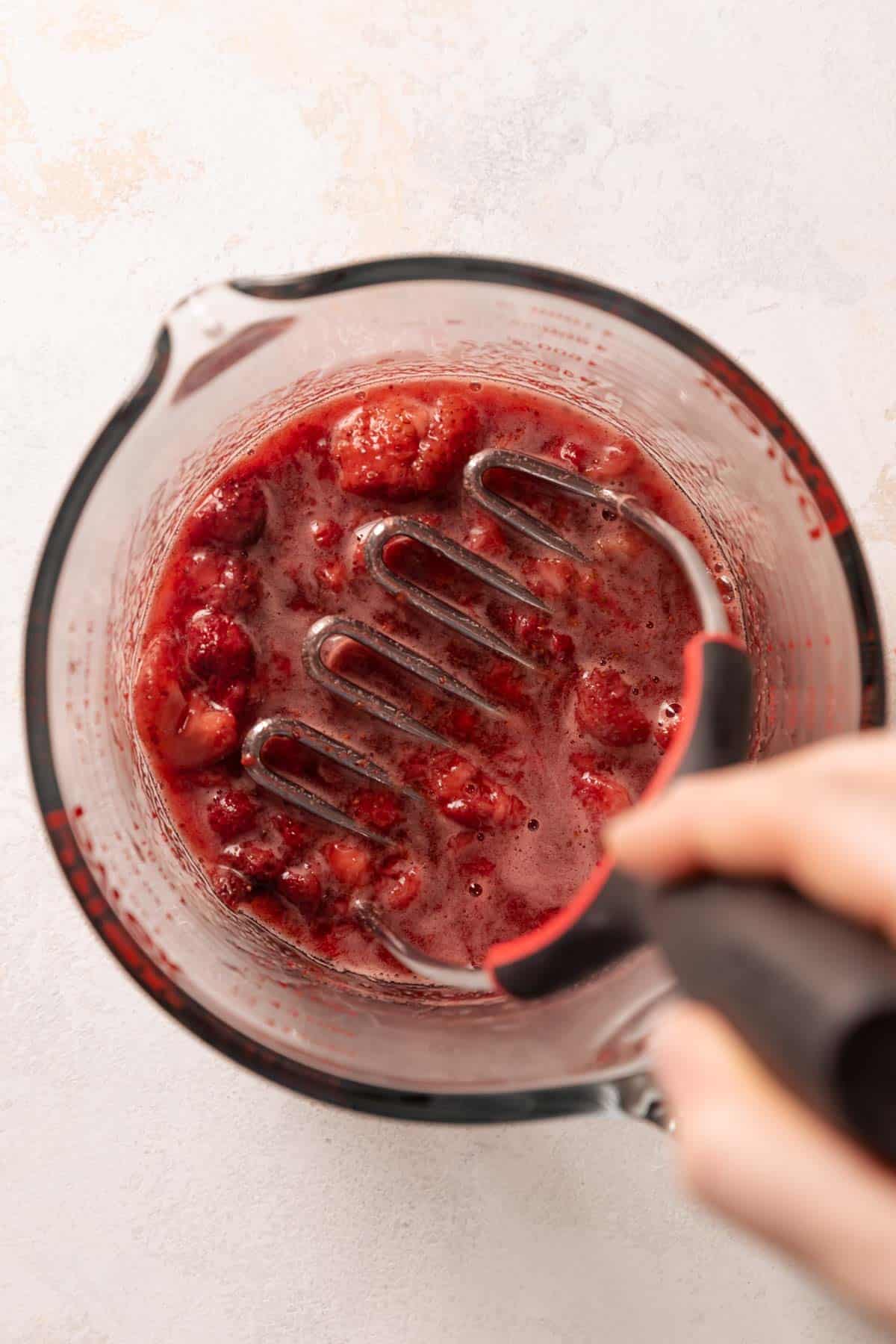 mashing roasted strawberries in a glass mixing bowl.