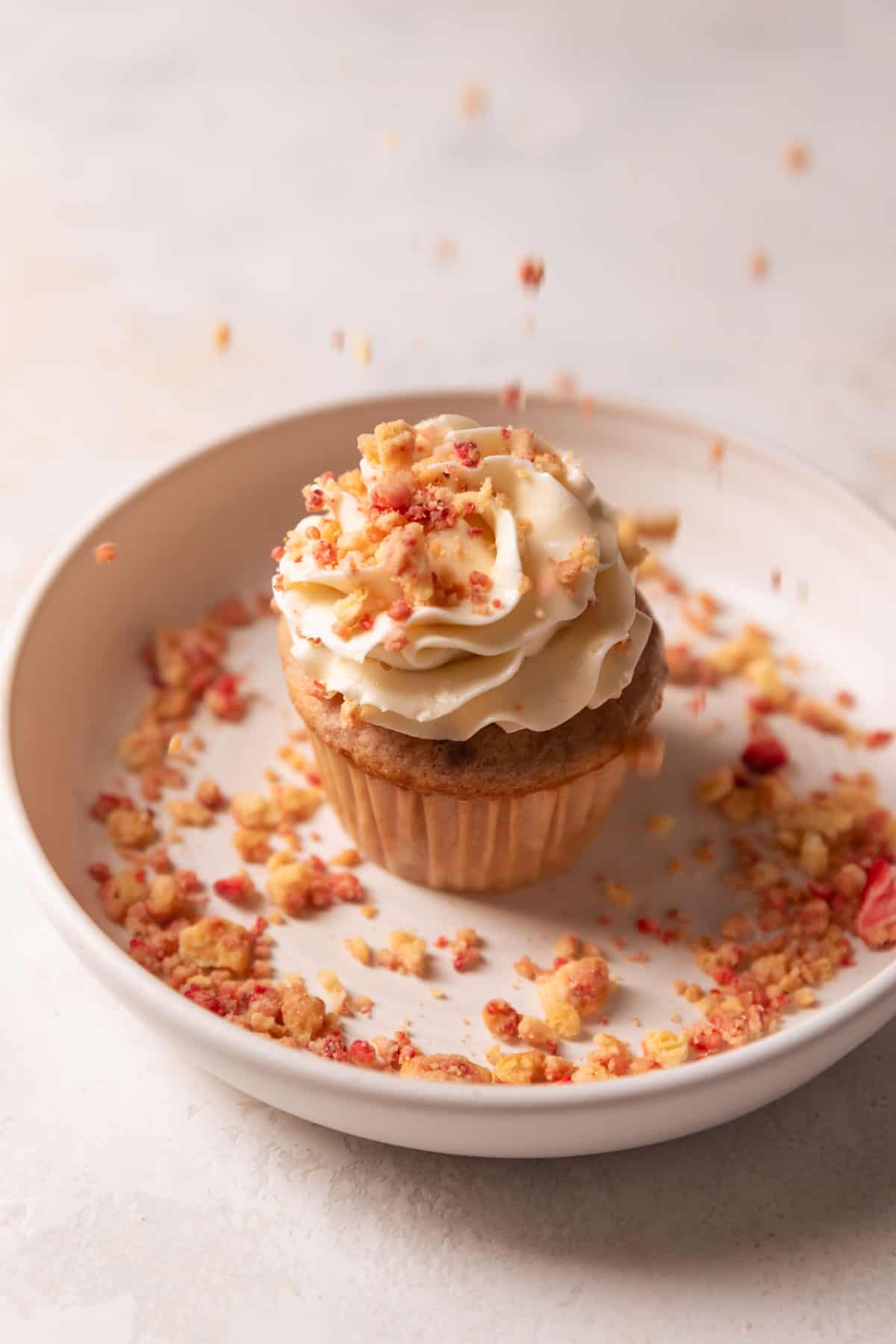 sprinkling the top of a cupcake with strawberry crunch topping.