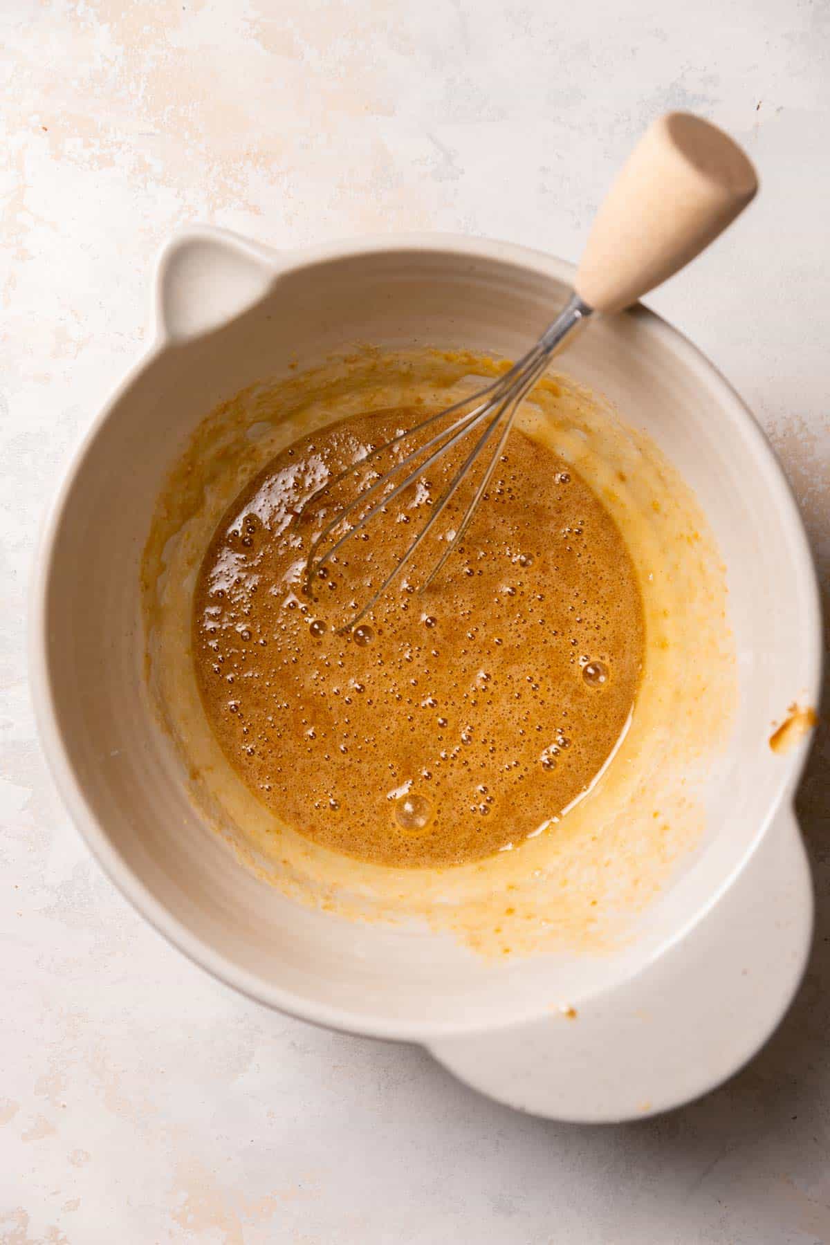 a mixing bowl with eggs, sugar, and vanilla being whisked.