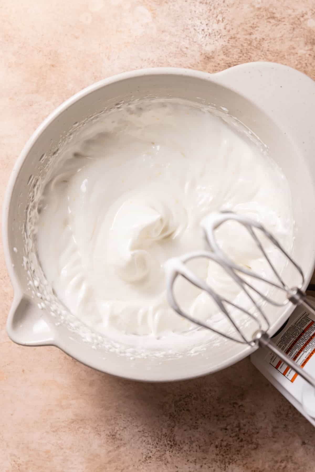 egg white meringue in a bowl with an electric mixer nearby.