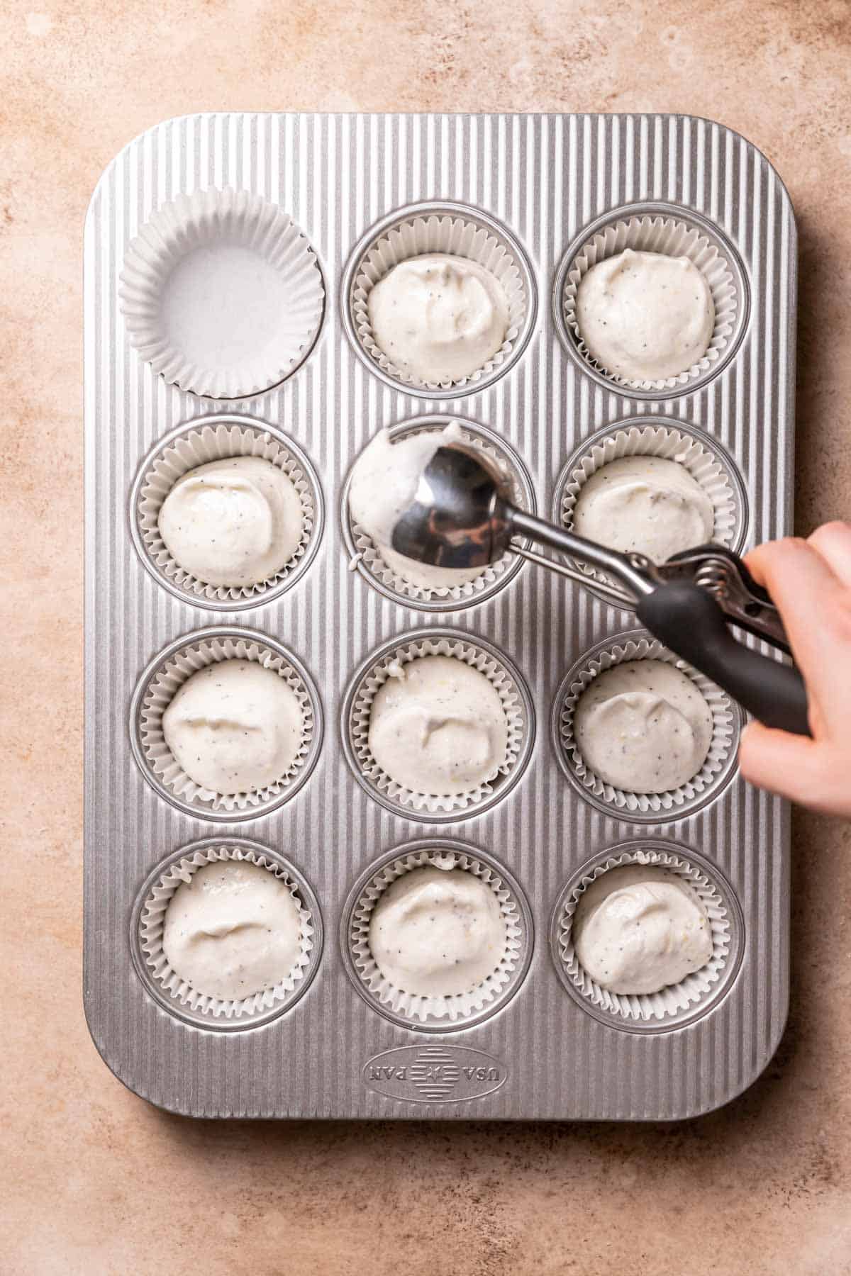 scooping cupcake batter into a lined cupcake tin.
