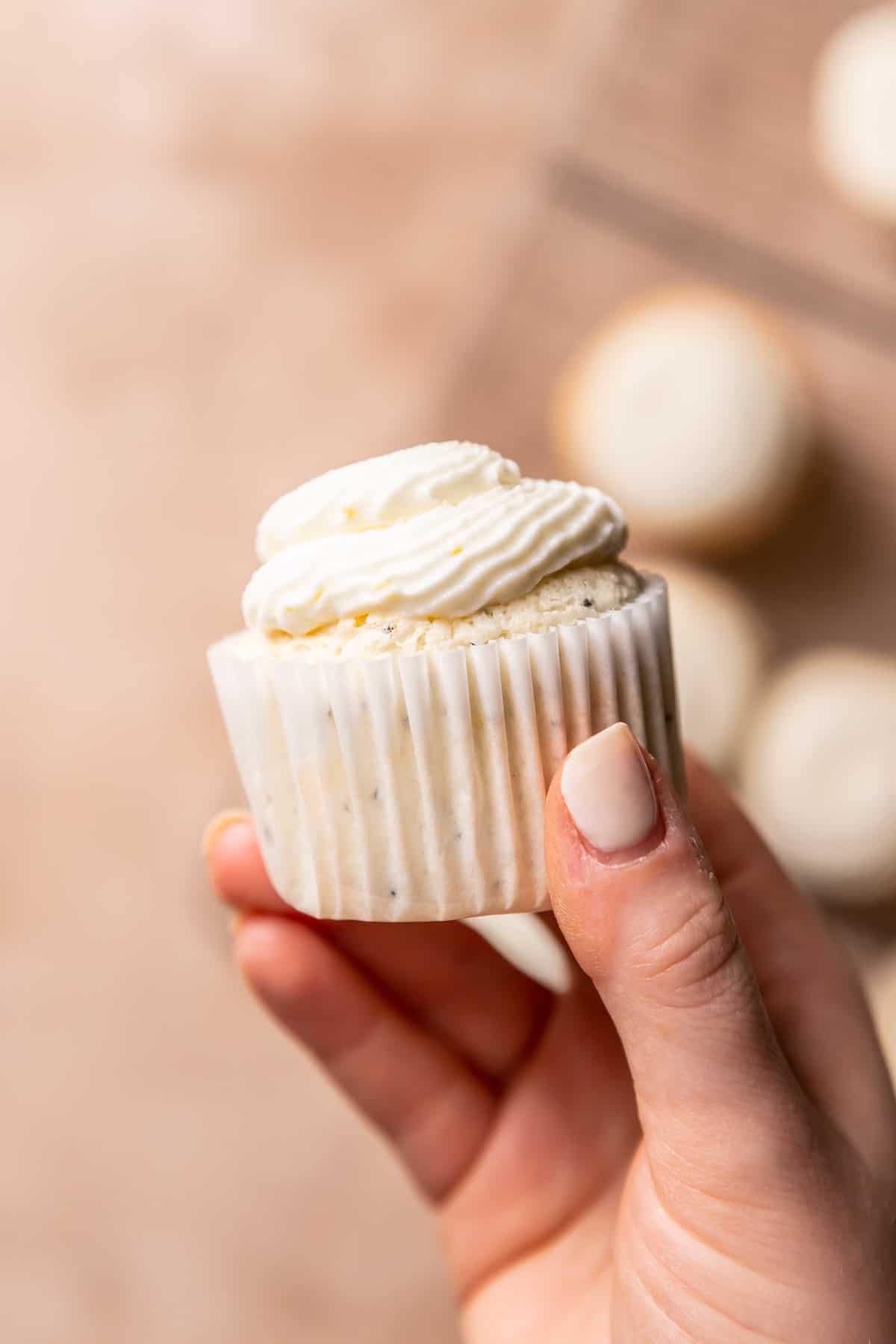 a hand holding a cupcake after it has been frosted