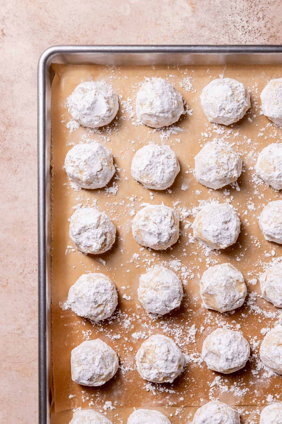cookie dough balls rolled in powdered sugar on a baking tray.
