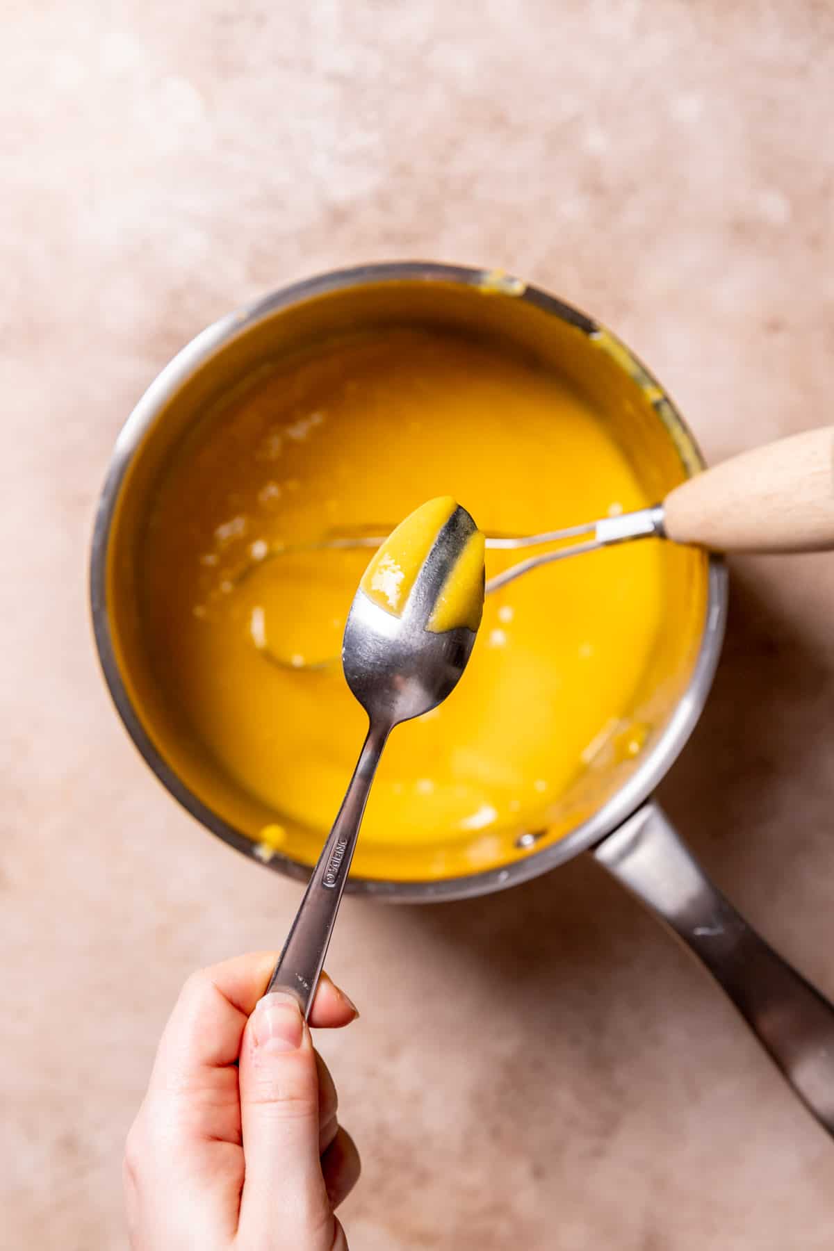 a spoon coated with mango curd to show that it is thick.