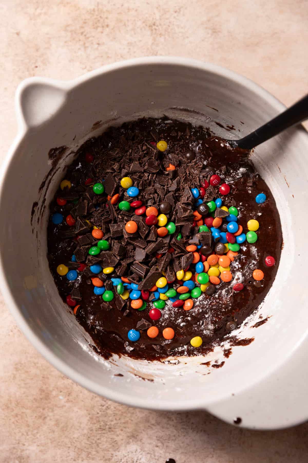 brownie batter in a bowl with mms and chocolate chunks on top.