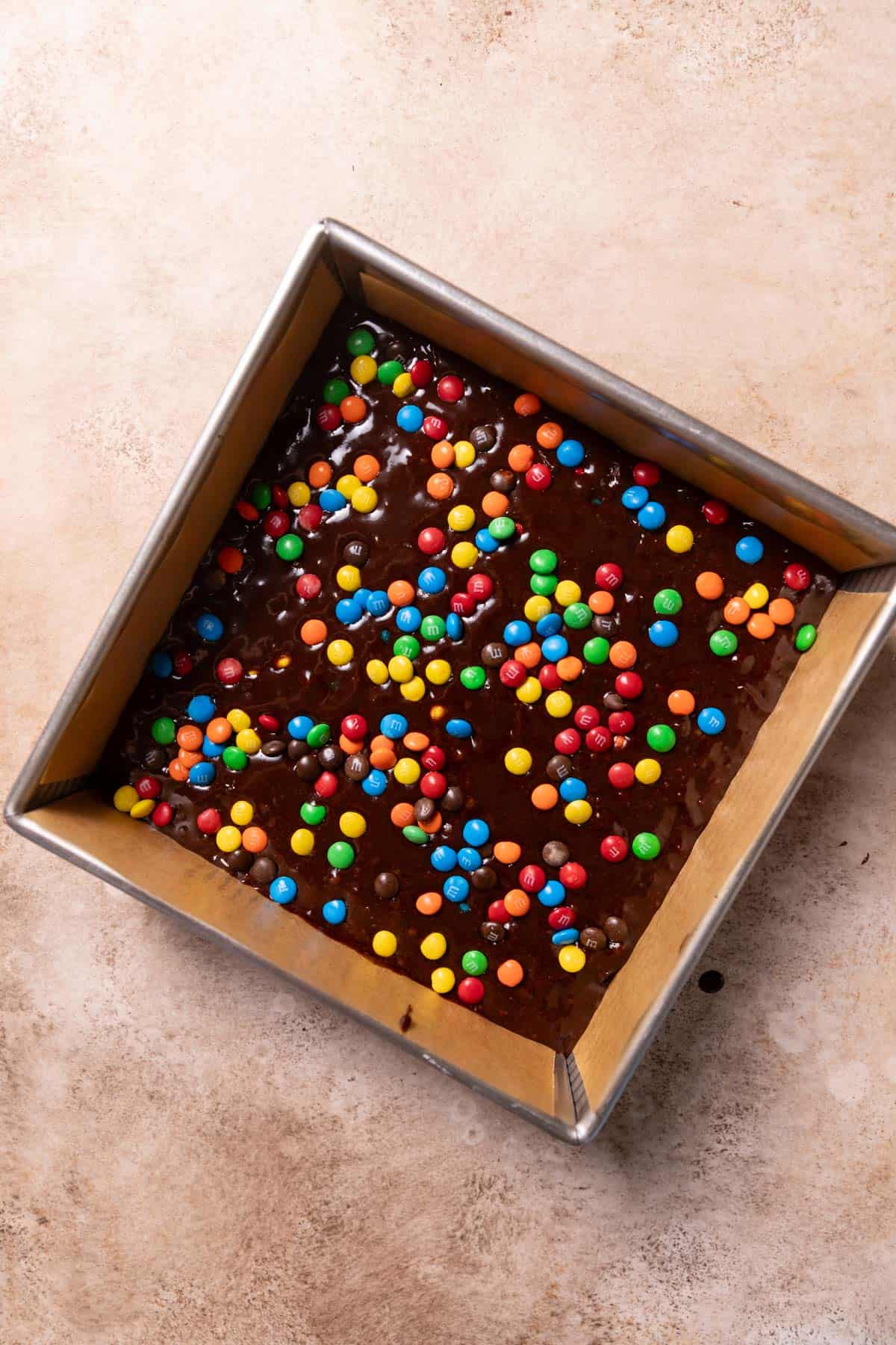 mm brownie batter in a pan with extra mm candies on top.