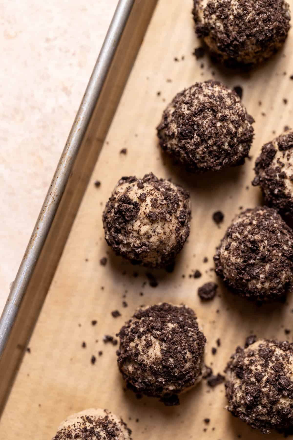 cookie dough balls rolled in oreo crumbs on a baking tray.